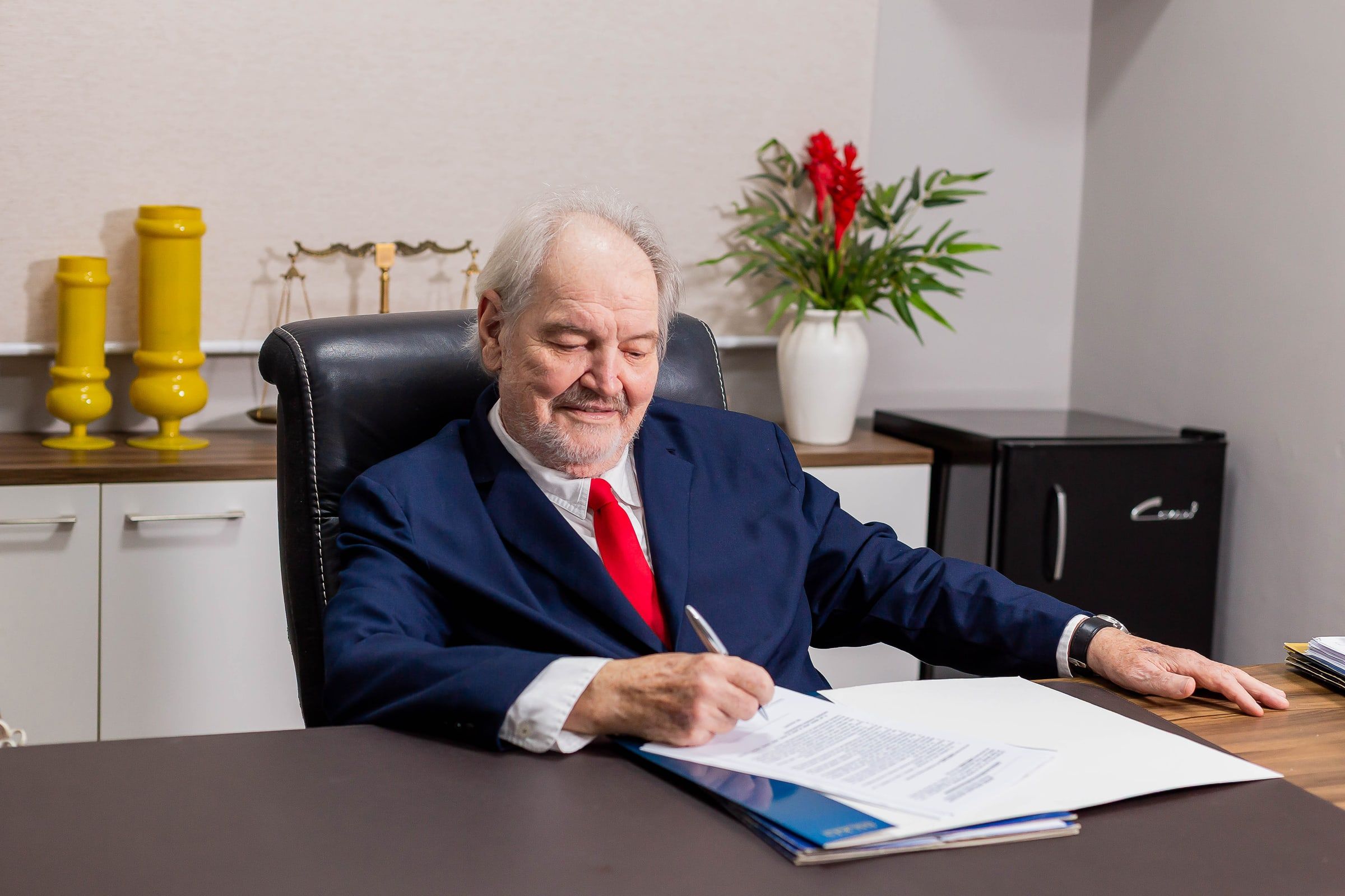 Dr. Elstor Backes revisa e assina documentos em sua mesa no escritório